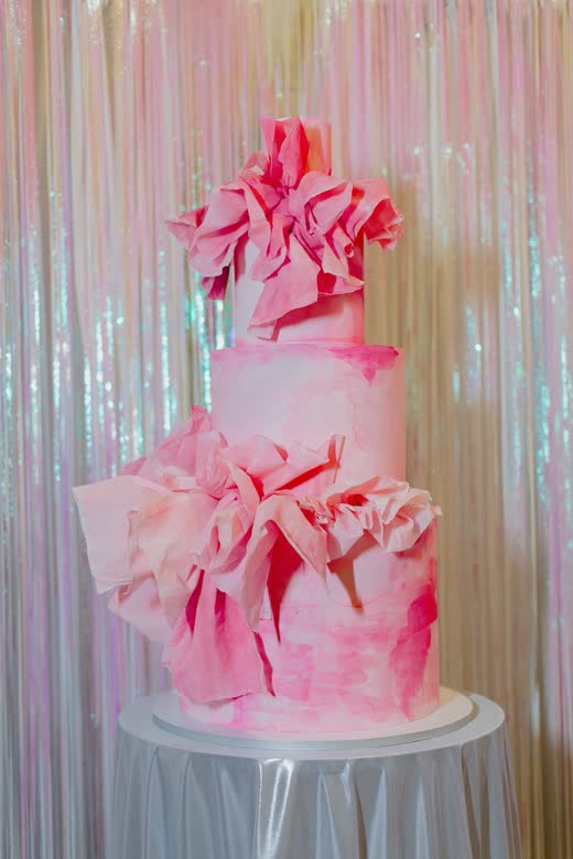 A pink ruffled cake against an iridescent curtain