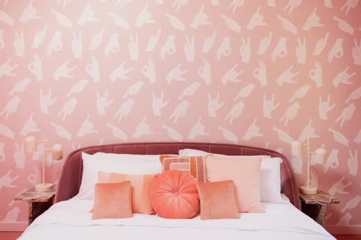 A pink bedroom with pink pillows and patterned wallpaper